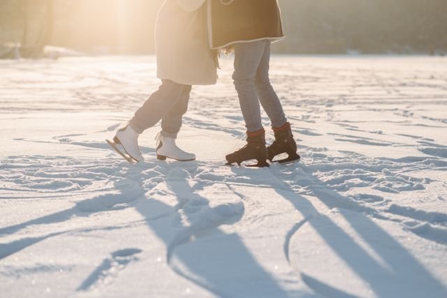 Closeup shot of two people in ice skates, presumably kissing while standing on a snow-covered surface.
